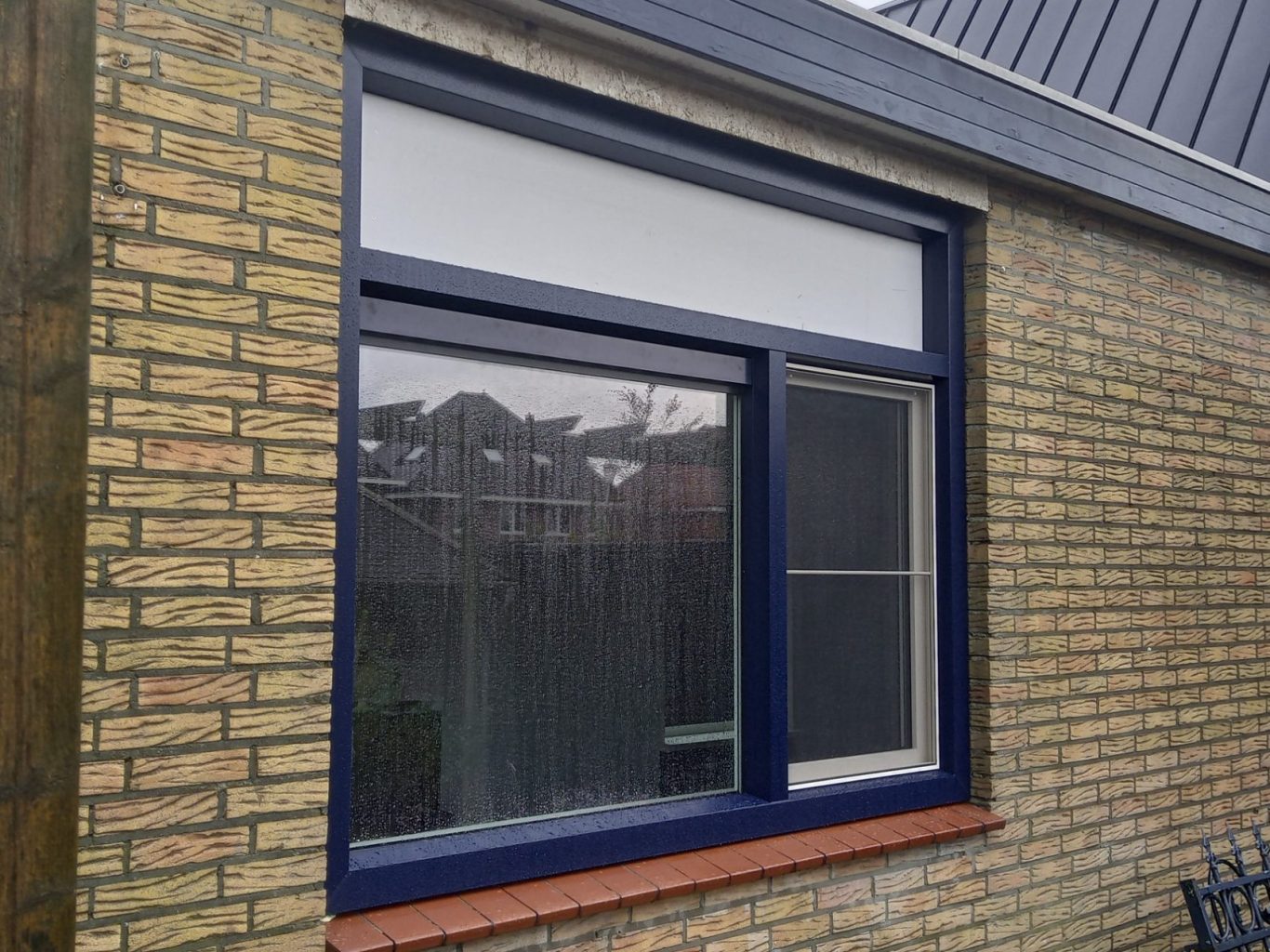 Blauwe raam omgeven door een stenen muur met een witte bovenpaneel.