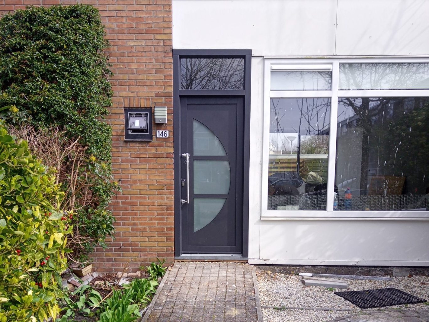 Zwarte deur met ronde glazen elementen naast een lichtbruine bakstenen muur.